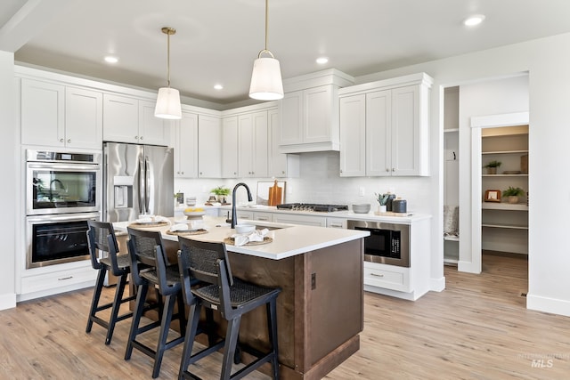 kitchen with appliances with stainless steel finishes, light countertops, light wood-style floors, a kitchen bar, and a sink