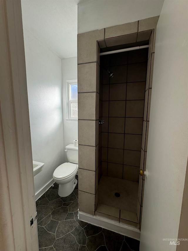 bathroom featuring a tile shower, tile patterned flooring, and toilet