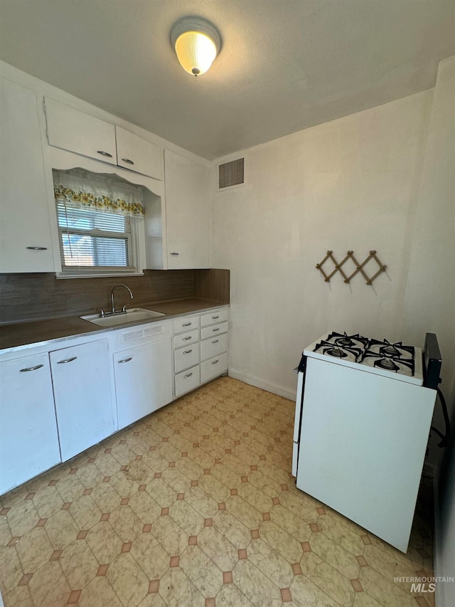 kitchen featuring white range with gas stovetop, sink, tasteful backsplash, and white cabinetry