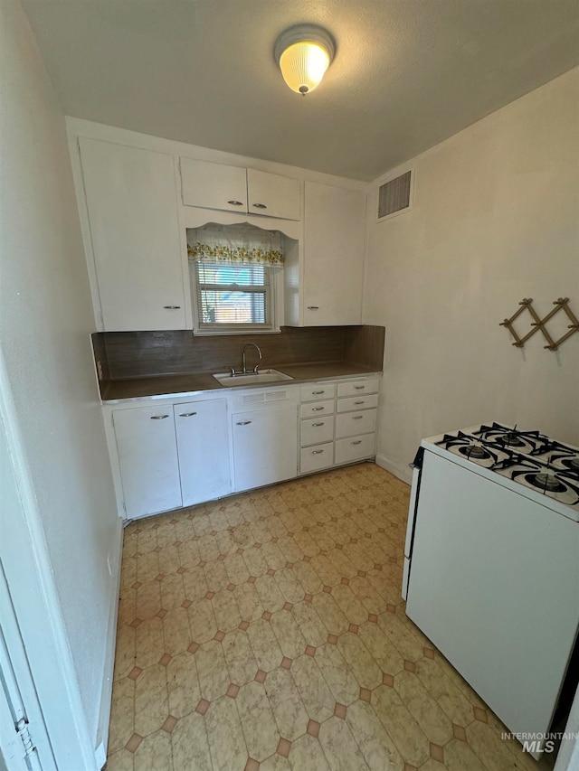 kitchen with white gas stove, white cabinetry, sink, and a textured ceiling