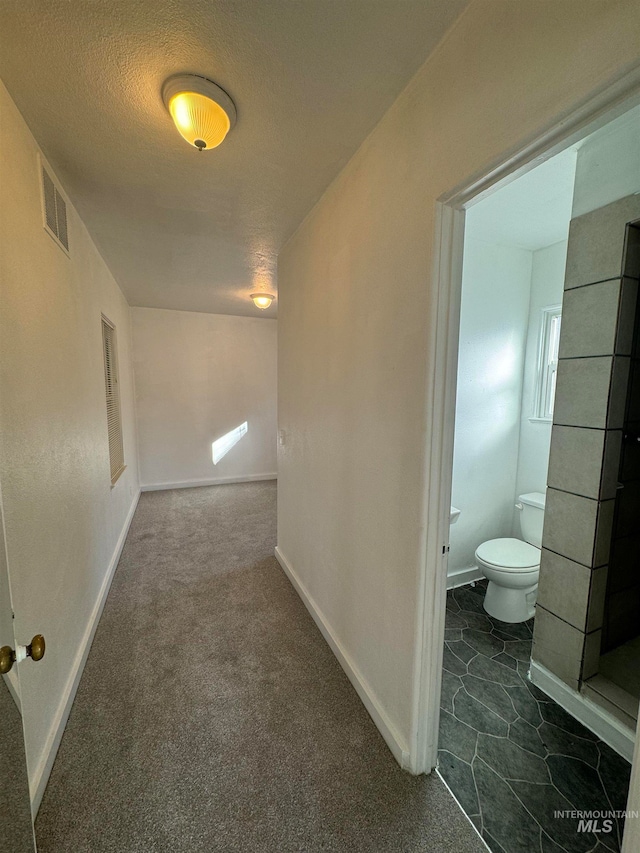 corridor featuring dark colored carpet and a textured ceiling