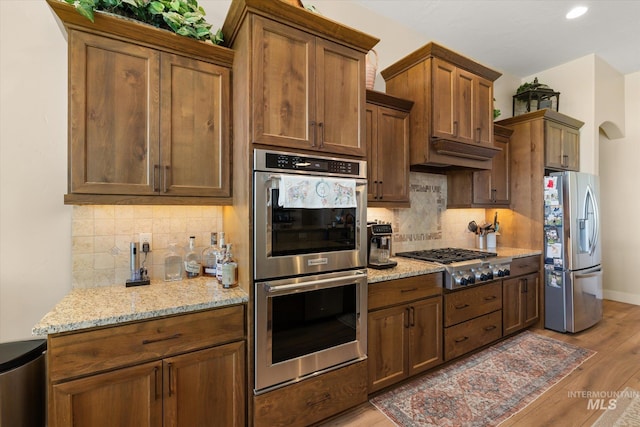 550 W Heikes Ln, Eagle, ID 83616 - kitchen featuring stainless steel appliances, light wood finished floors, tasteful backsplash, light stone counters, and recessed lighting