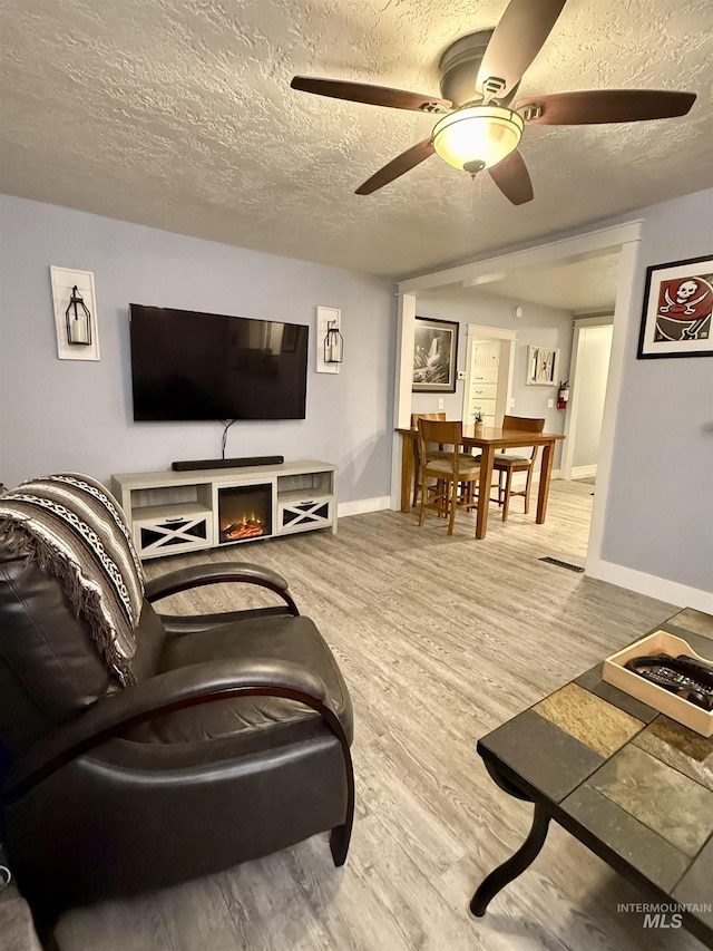 living room with ceiling fan, wood-type flooring, and a textured ceiling