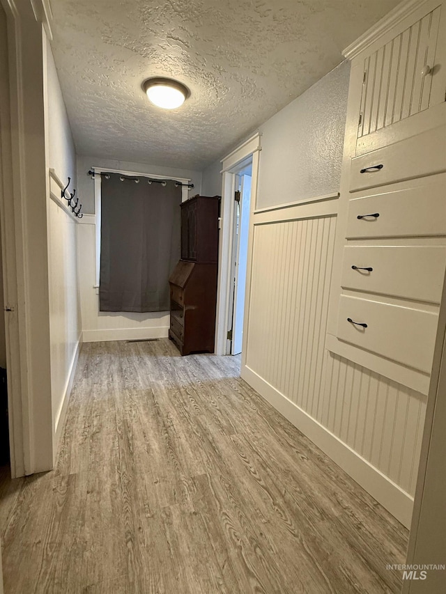 hall with a textured ceiling and light hardwood / wood-style floors