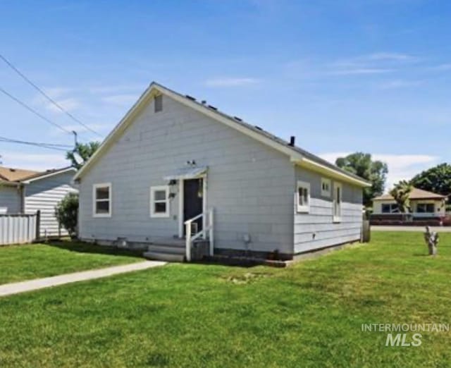 back of property with entry steps, a lawn, and fence