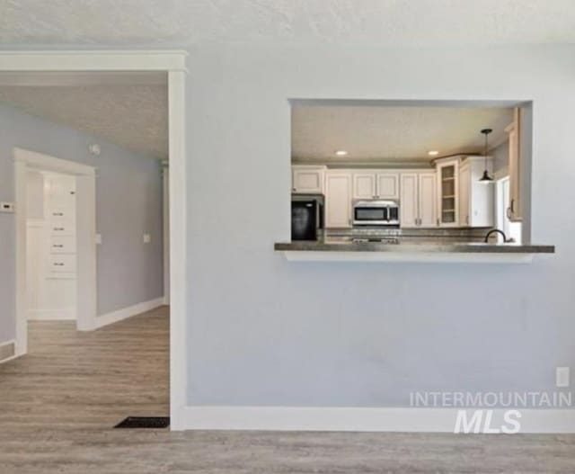 kitchen with hanging light fixtures, kitchen peninsula, refrigerator, a textured ceiling, and light wood-type flooring