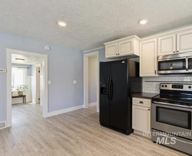 kitchen with backsplash, cream cabinets, light hardwood / wood-style flooring, a textured ceiling, and stainless steel appliances