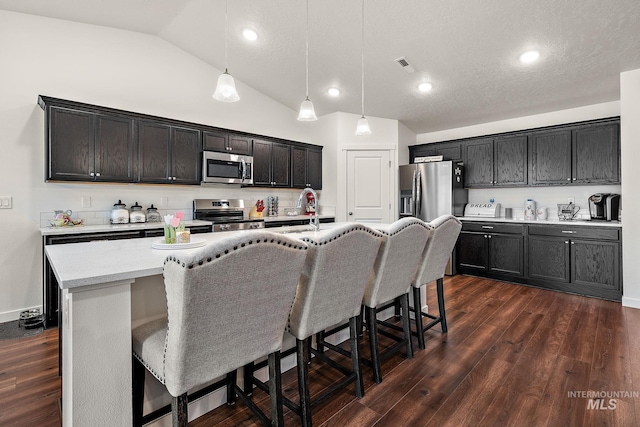 2701 N Ice Fire Pl, Star, ID 83669 - kitchen featuring appliances with stainless steel finishes, lofted ceiling, a kitchen bar, dark wood-style floors, and hanging light fixtures