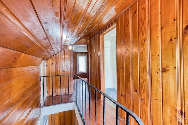 hallway featuring lofted ceiling, an upstairs landing, wooden walls, and wood ceiling