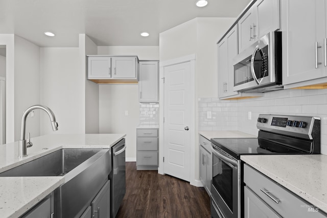 kitchen with stainless steel appliances, light stone counters, dark wood-style flooring, and a sink