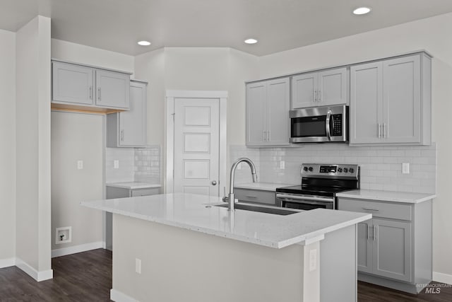 kitchen featuring dark wood finished floors, light stone counters, appliances with stainless steel finishes, gray cabinets, and a sink