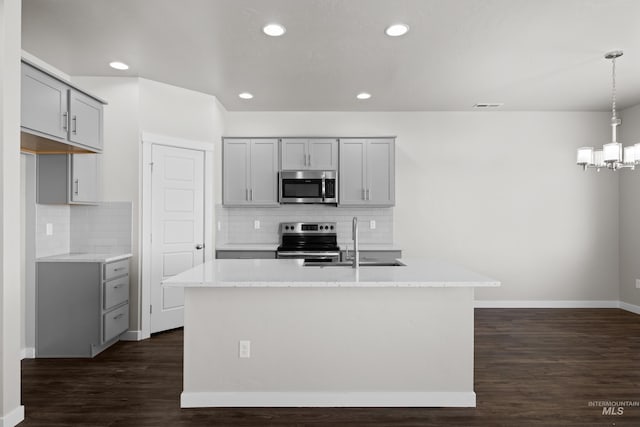 kitchen with dark wood-style flooring, stainless steel appliances, gray cabinetry, a kitchen island with sink, and a sink