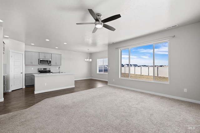 unfurnished living room featuring ceiling fan with notable chandelier, dark colored carpet, visible vents, and baseboards