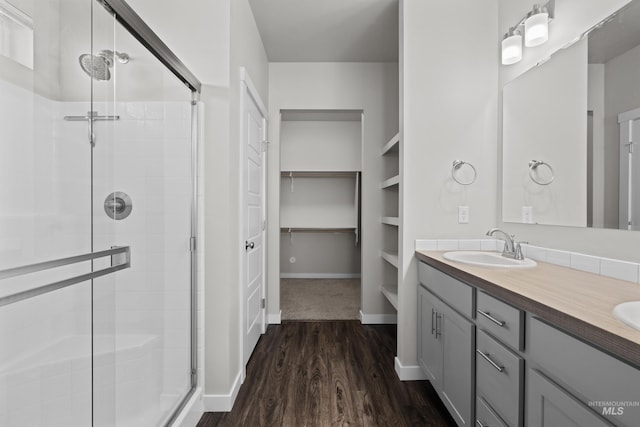 full bathroom with wood finished floors, a sink, baseboards, a shower stall, and double vanity