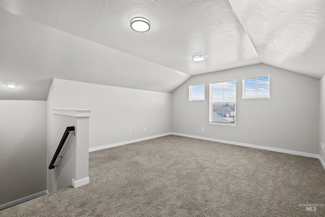 additional living space with a textured ceiling, carpet floors, vaulted ceiling, and baseboards