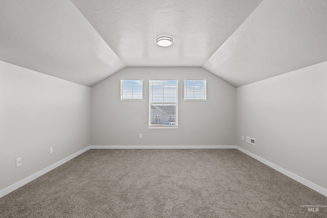 additional living space featuring a textured ceiling, lofted ceiling, visible vents, and baseboards