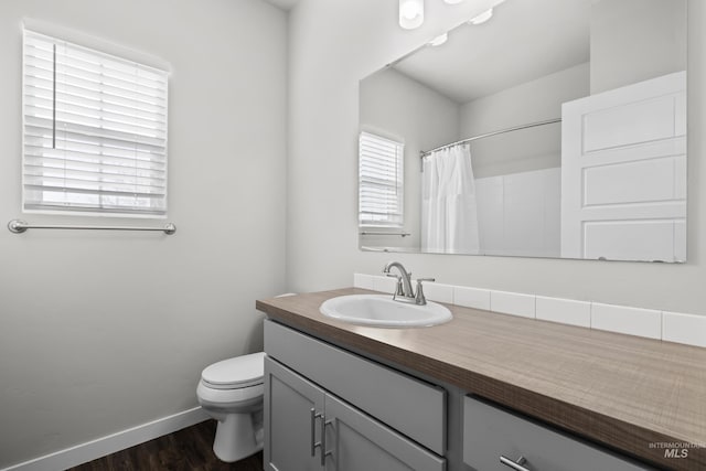 full bathroom with curtained shower, toilet, vanity, wood finished floors, and baseboards