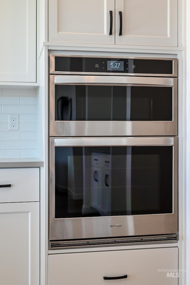 interior details with white cabinetry, double oven, and decorative backsplash