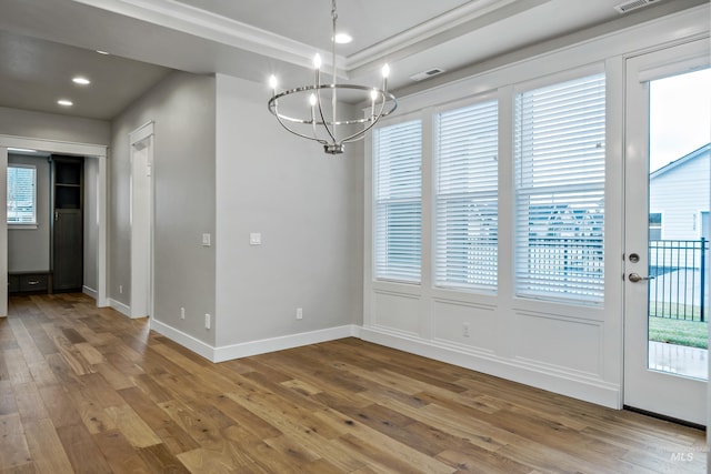 unfurnished dining area with a chandelier, hardwood / wood-style floors, and ornamental molding