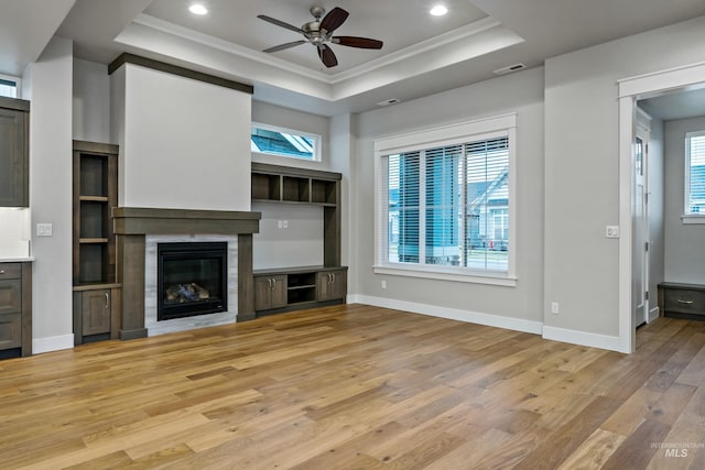 unfurnished living room featuring a tray ceiling, crown molding, ceiling fan, and light hardwood / wood-style floors