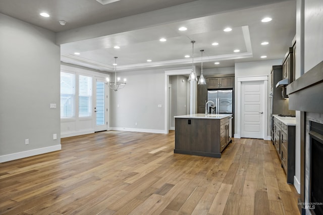 kitchen with a raised ceiling, dark brown cabinetry, a center island with sink, and pendant lighting