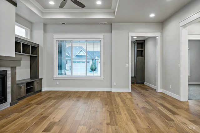 unfurnished living room featuring a tray ceiling, ceiling fan, crown molding, and light wood-type flooring