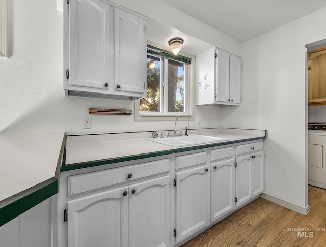 kitchen with washer / dryer, a sink, light wood-style floors, white cabinetry, and light countertops
