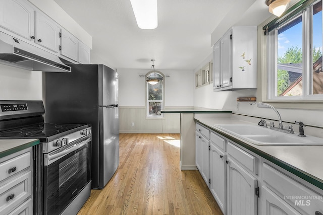 kitchen featuring stainless steel electric range, under cabinet range hood, healthy amount of natural light, white cabinetry, and wainscoting