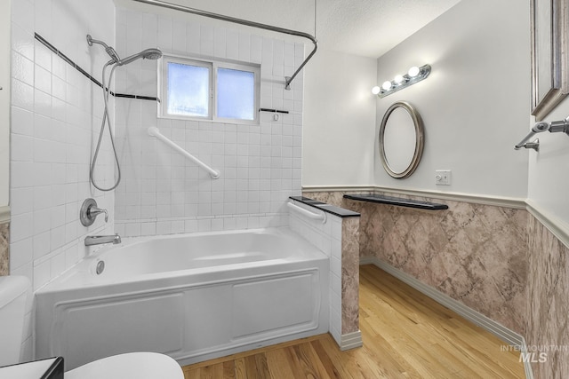 full bath with wainscoting, toilet, wood finished floors, and shower / bath combination