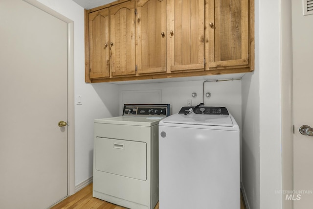 laundry room featuring washer and clothes dryer, cabinet space, light wood-style flooring, and baseboards
