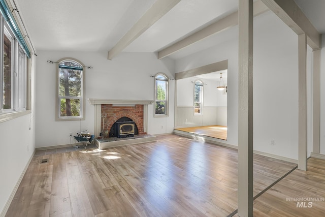 unfurnished living room featuring wood-type flooring, plenty of natural light, beam ceiling, wainscoting, and baseboards