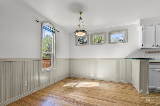 unfurnished dining area with light wood finished floors and wainscoting