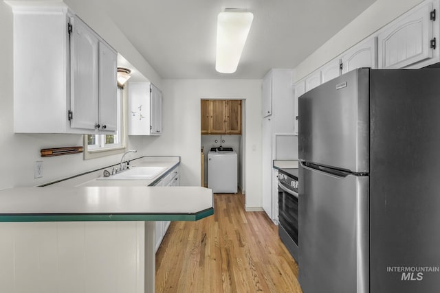 kitchen with freestanding refrigerator, washer / clothes dryer, a sink, a peninsula, and light wood finished floors