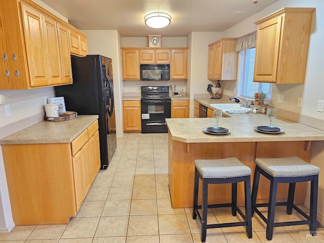 kitchen featuring sink, kitchen peninsula, a breakfast bar, light tile patterned floors, and black appliances