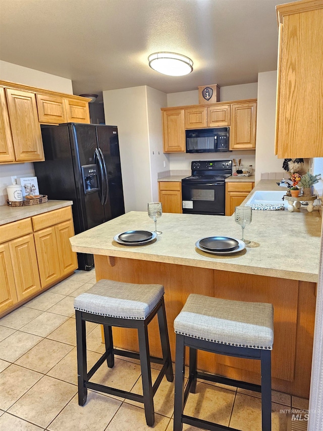 kitchen featuring a kitchen bar, kitchen peninsula, sink, black appliances, and light tile patterned floors