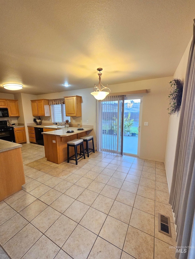 kitchen with hanging light fixtures, kitchen peninsula, a breakfast bar, light tile patterned floors, and black appliances