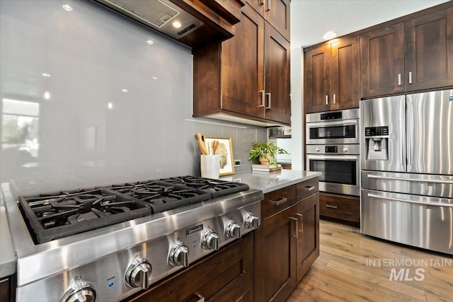 5085 S Taboo Pl, Boise, ID 83716 - kitchen with stainless steel appliances, light wood finished floors, dark brown cabinetry, light stone counters, and custom range hood