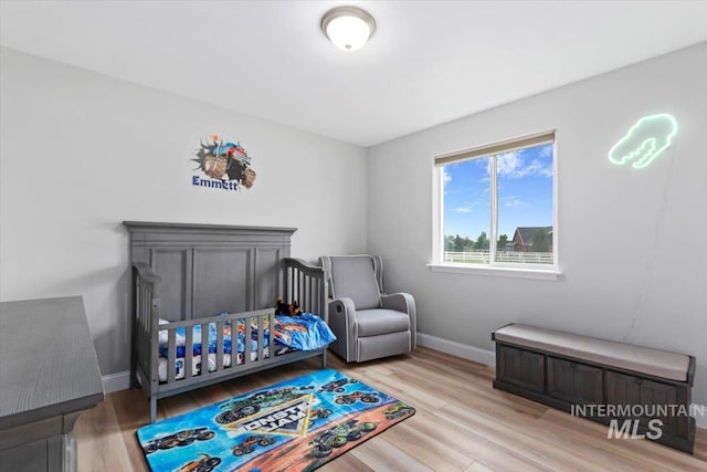 bedroom with a nursery area, baseboards, and wood finished floors