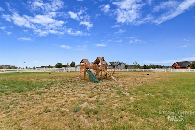 view of playground with fence, a lawn, and a rural view