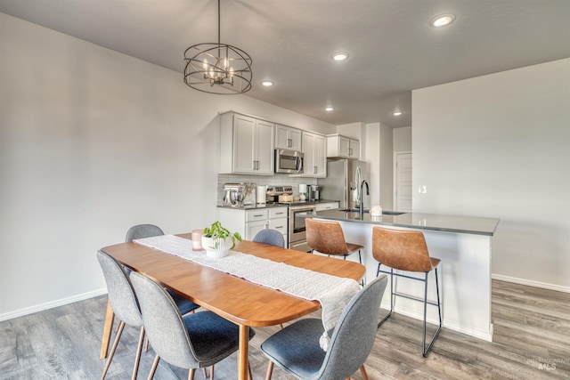 dining space with light wood finished floors, recessed lighting, an inviting chandelier, and baseboards