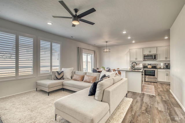 living room featuring light wood-style flooring, a textured ceiling, recessed lighting, baseboards, and ceiling fan