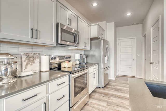 kitchen featuring baseboards, light wood-type flooring, decorative backsplash, recessed lighting, and appliances with stainless steel finishes