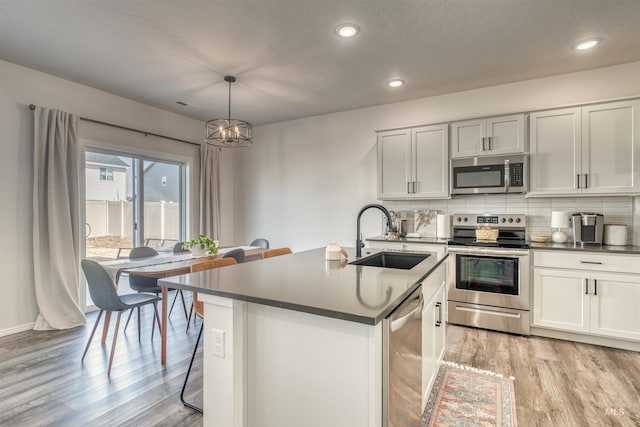 kitchen featuring an island with sink, a sink, backsplash, light wood-style floors, and appliances with stainless steel finishes