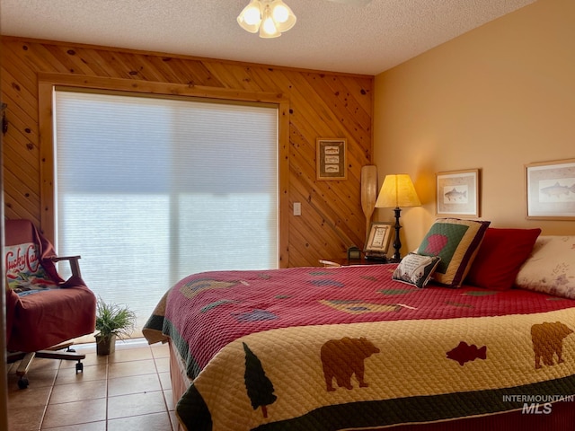 bedroom featuring light tile patterned flooring, wooden walls, and a textured ceiling