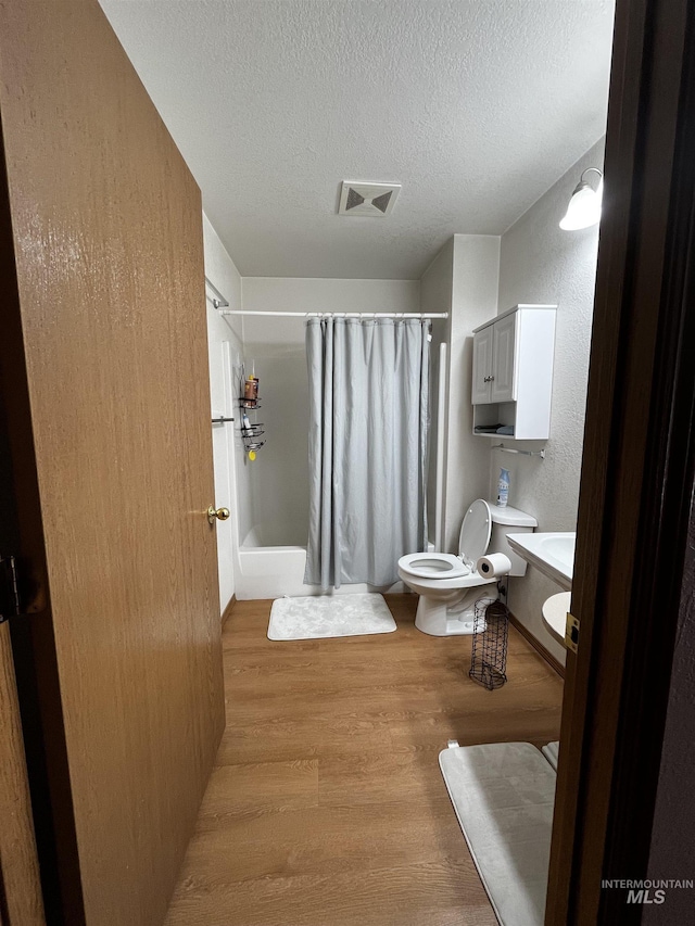 full bath featuring toilet, a textured ceiling, a shower with shower curtain, wood finished floors, and visible vents