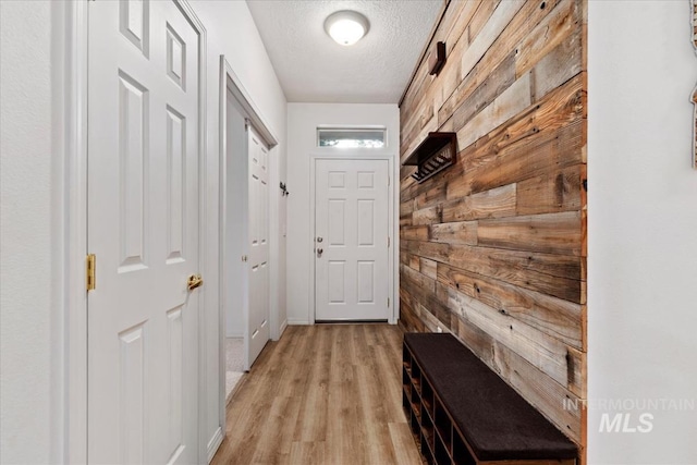 mudroom featuring wooden walls, light hardwood / wood-style floors, and a textured ceiling