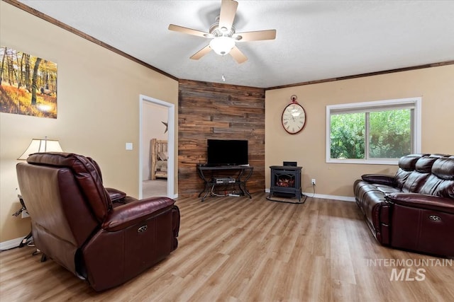 living room with ornamental molding, a wood stove, ceiling fan, and light hardwood / wood-style floors