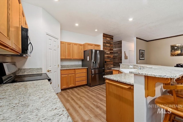 kitchen featuring sink, stainless steel appliances, light stone countertops, a kitchen bar, and light wood-type flooring