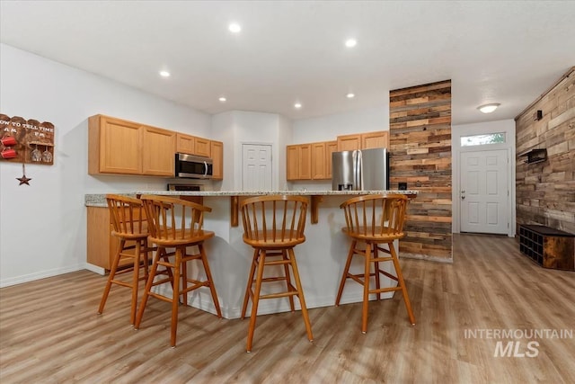 kitchen featuring a breakfast bar, stainless steel appliances, light stone countertops, light brown cabinets, and light wood-type flooring