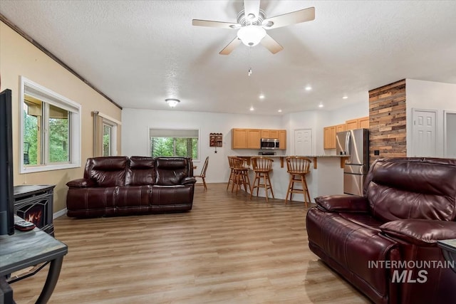 living room with ceiling fan, light wood-type flooring, a textured ceiling, and a wood stove